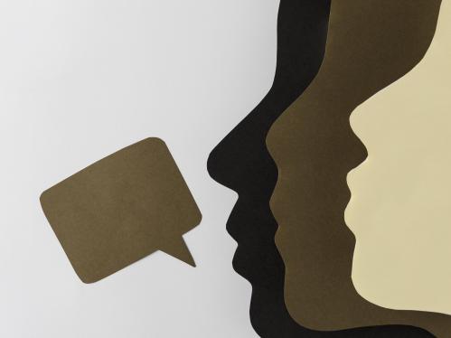 Paper cut outs of different colored faces with a speech bubble