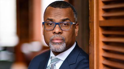 Eddie S. Glaude Jr. Closeup of an African American man with a white goatie wearing blue rimmed glasses and a royal blue suit.