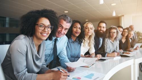 Diverse team of professionals in an office setting with the focus on a smiling african american woman in front wearing a silk grey blouse