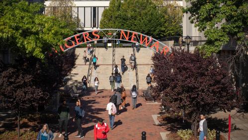 Students walking under an iron archway with the words Rutgers Newark in Red