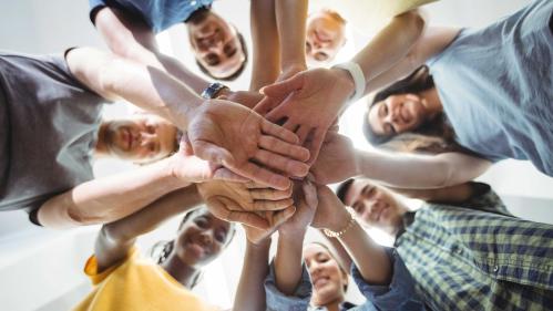 AN upward shot of business executives from diverse backgrounds with their hand stacked looking down and smiling