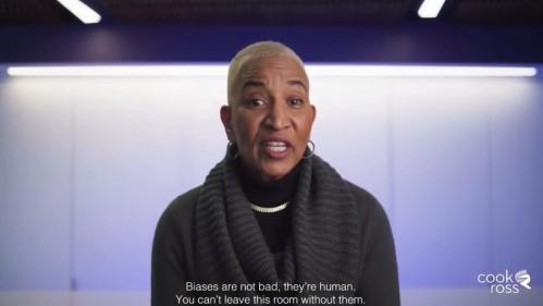 These is a screenshot of the PAUSE bias video. It features an african american woman with short blond hair wearing a black sweater. She is sitting in front of a purple wall.