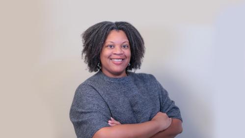 Dr. Melissa Wooten smiles in front of a neutral background with arms casually folded
