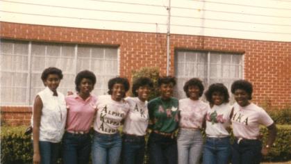 Group of eight Black women from Alpha Kappa Alpha Sorority standing in from of building