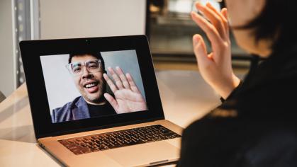 A woman waving on a virtual call with a male mentor. They are waving at each other.