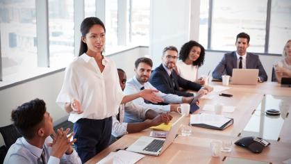 Woman standing at conference table and presenting to colleagues
