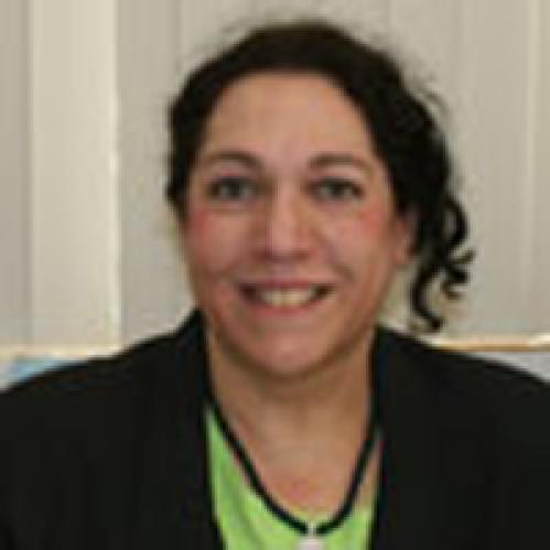 A jewish woman with curly hair smiling. She is wearing a lime green blouse with a black jacket