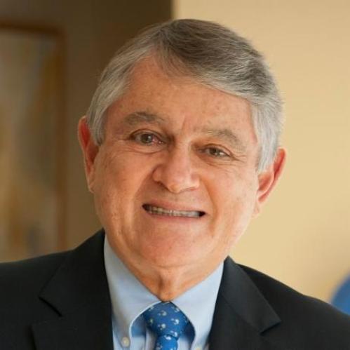 Javier Escobar is an older man with short grey hair wearing a light blue collared shirt, blue tie and black jacket