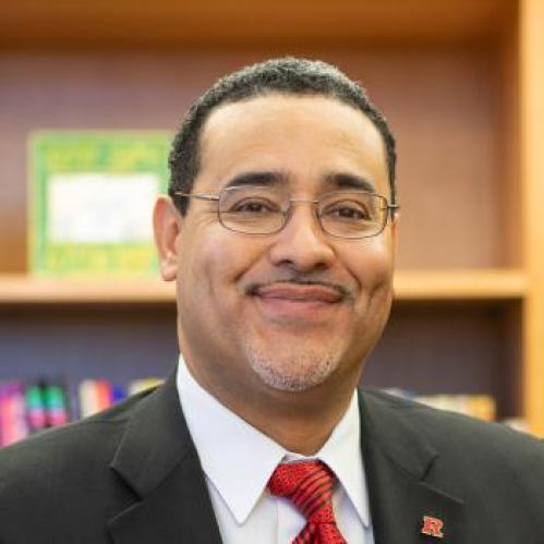 Salvador is a hispanic man. He is smiling and wearing glasses with a white collared tshirt, red tshirt and grey jacket
