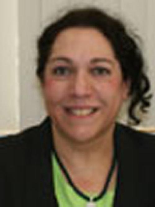 A jewish woman with curly hair smiling. She is wearing a lime green blouse with a black jacket