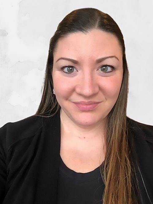 Christie Howley - A  caucasian woman with straight brown long hair looking ahead. She is smiling and wearing a black blouse and jacket and she is standing in front of a white background.