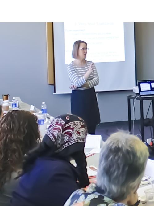 An Oasis workshop in a large conference room with a diverse group of women with a female lecturer standing at the front of the room talking