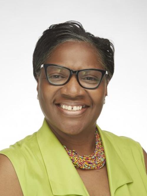 Sharon Stroye is an african american woman with short straightened hair. She is smiling and wearing black rimmed glasses and colorful beaded necklace and a lime green shirt
