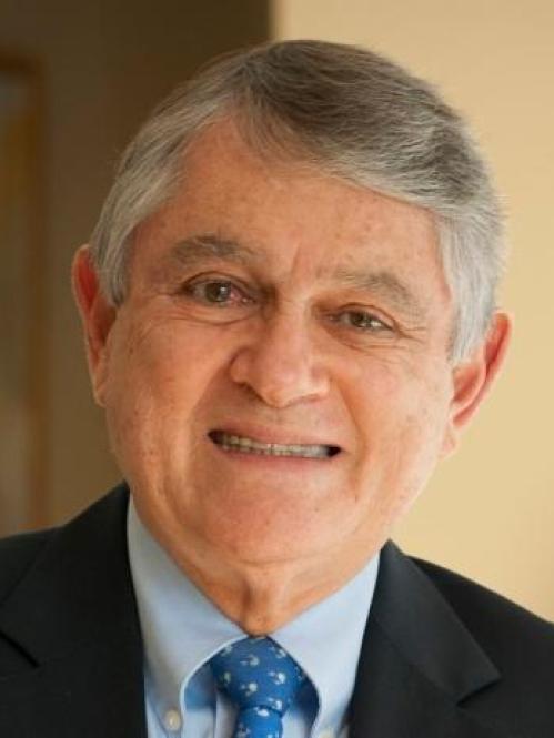 Javier Escobar is an older man with short grey hair wearing a light blue collared shirt, blue tie and black jacket