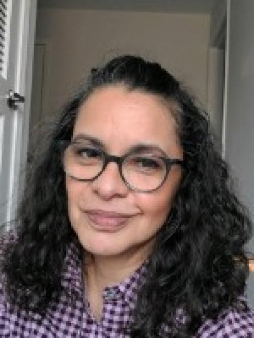 Nancy has wavy black hair and wearing a plaid shirt.