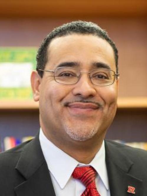 Salvador is a hispanic man. He is smiling and wearing glasses with a white collared tshirt, red tshirt and grey jacket