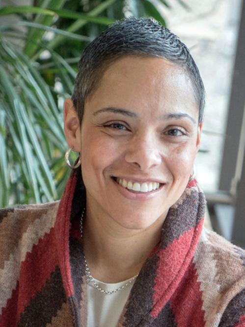 Marta has short cropped hair and she is wearing a multicolored red sweater.