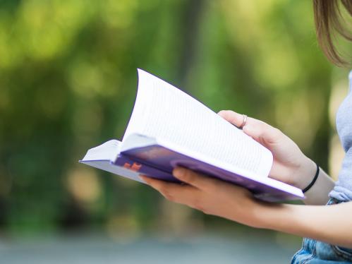 closeup of a woman's hand turning the pages of a book with trees in the background