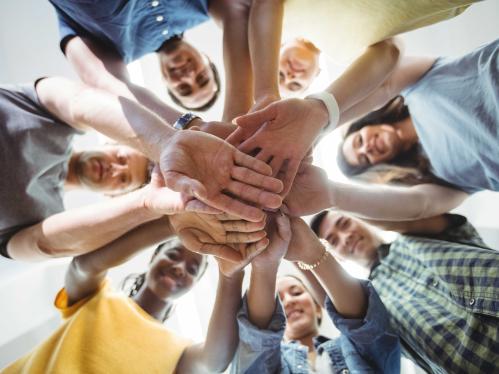 AN upward shot of business executives from diverse backgrounds with their hand stacked looking down and smiling