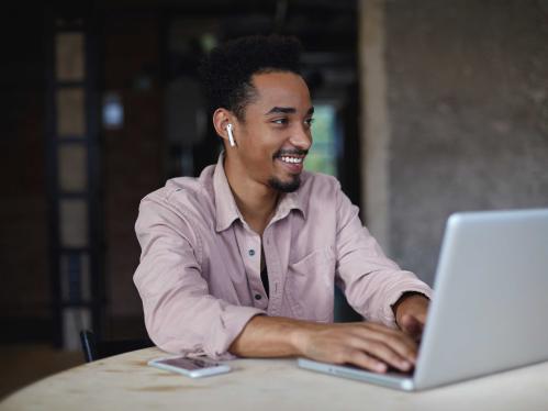 cheerful-dark-skinned-male-with-short-haircut-beige-shirt-working-modern-office-with-laptop-typing-text-with-hands-keyboard