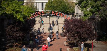 Students walking under an iron archway with the words Rutgers Newark in Red